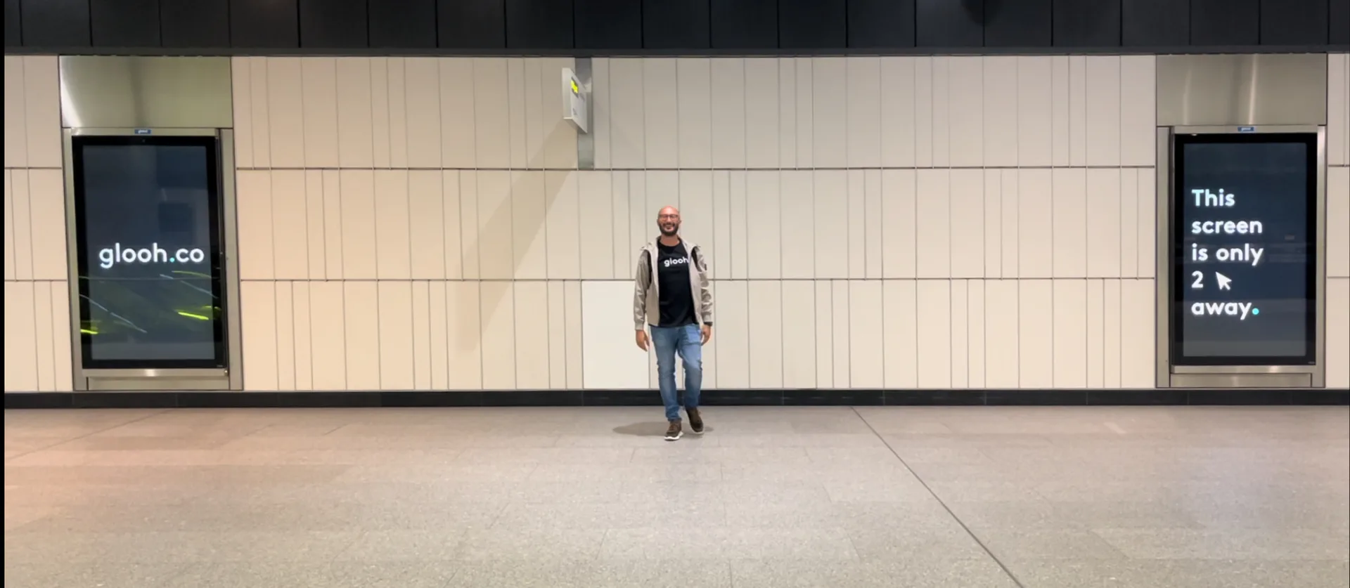 Dimitri Themelis en t-shirt glooh, dans une gare, entre deux écrans qui diffusent la campagne de glooh