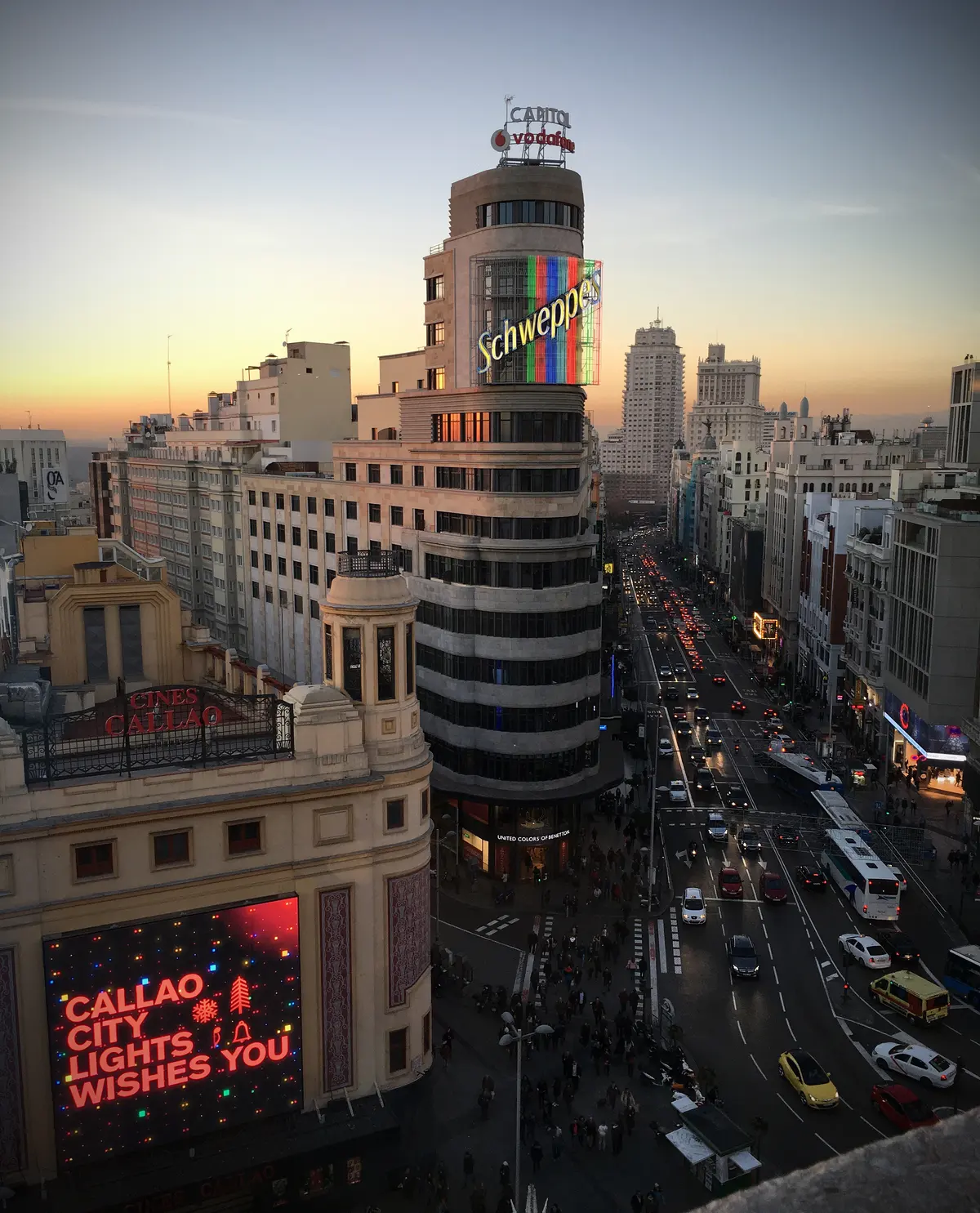 The Schweppes neon on the Edificio Carrión above Plaza del Callao at dusk, with Gran Vía running west towards Plaza de España