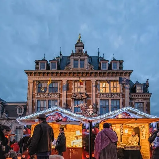 Christmas market chalets in front of a historic building in Namur at dusk