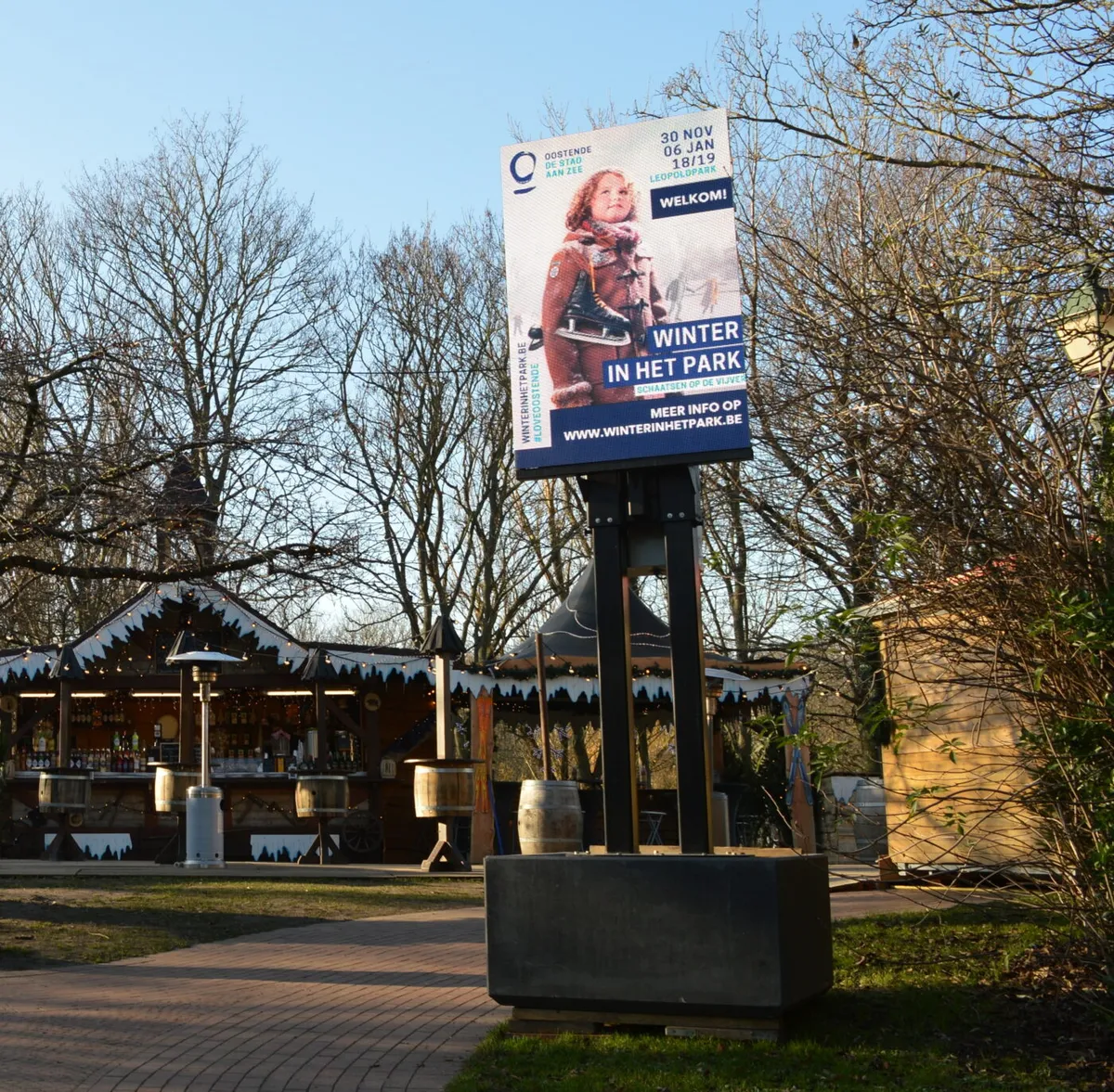 Portrait LED screen on a pole between the chalets of Winter in het Park, Leopoldpark, Ostend